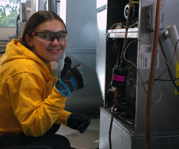 HVAC student at Pinnacle Career Institute working on HVAC equipment looking at the camera smiling and giving a thumbs up
